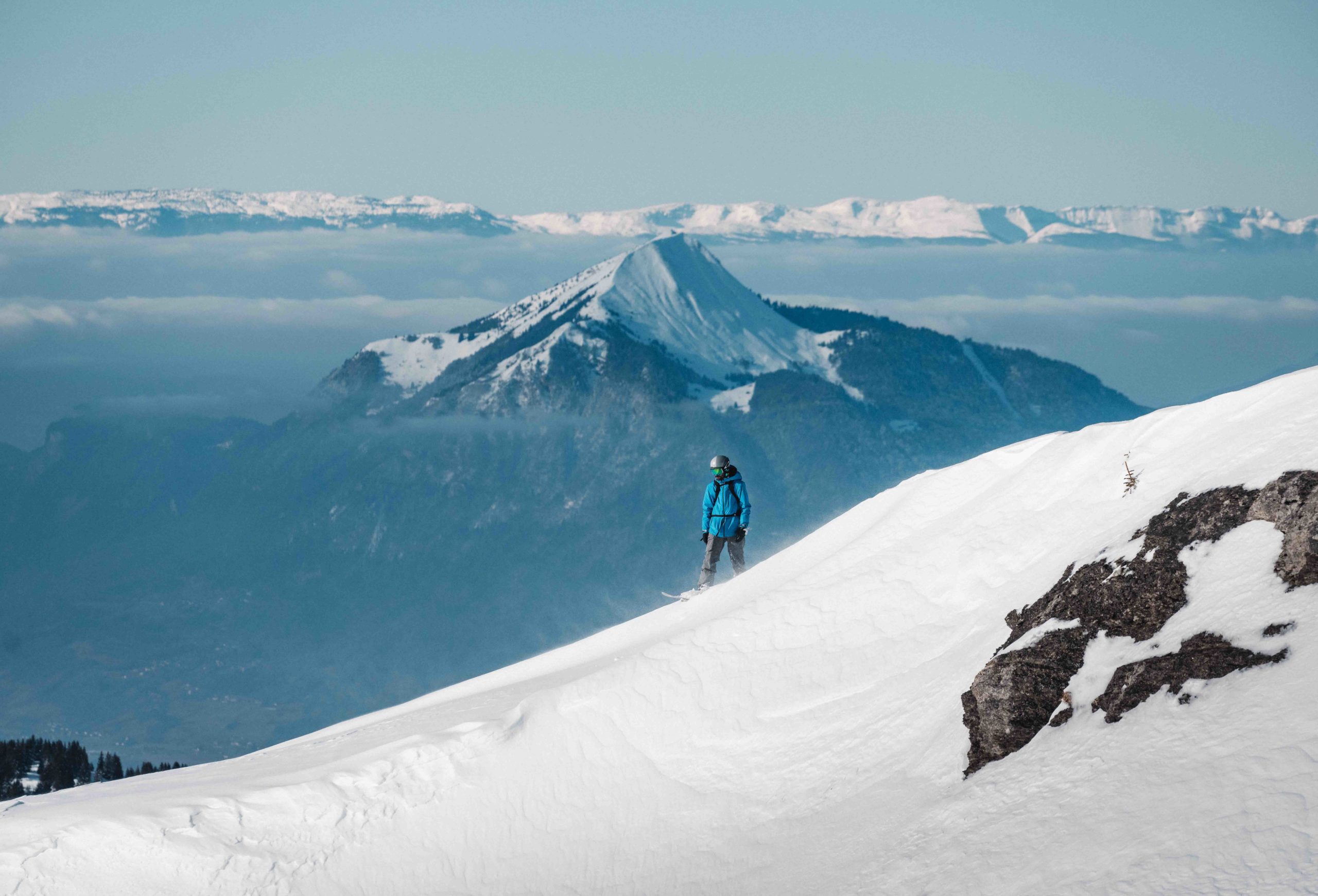 Flaine- Un snowboardeur sur une pente de neige poudreuse avec la montagne le Môle en arrière-plan.