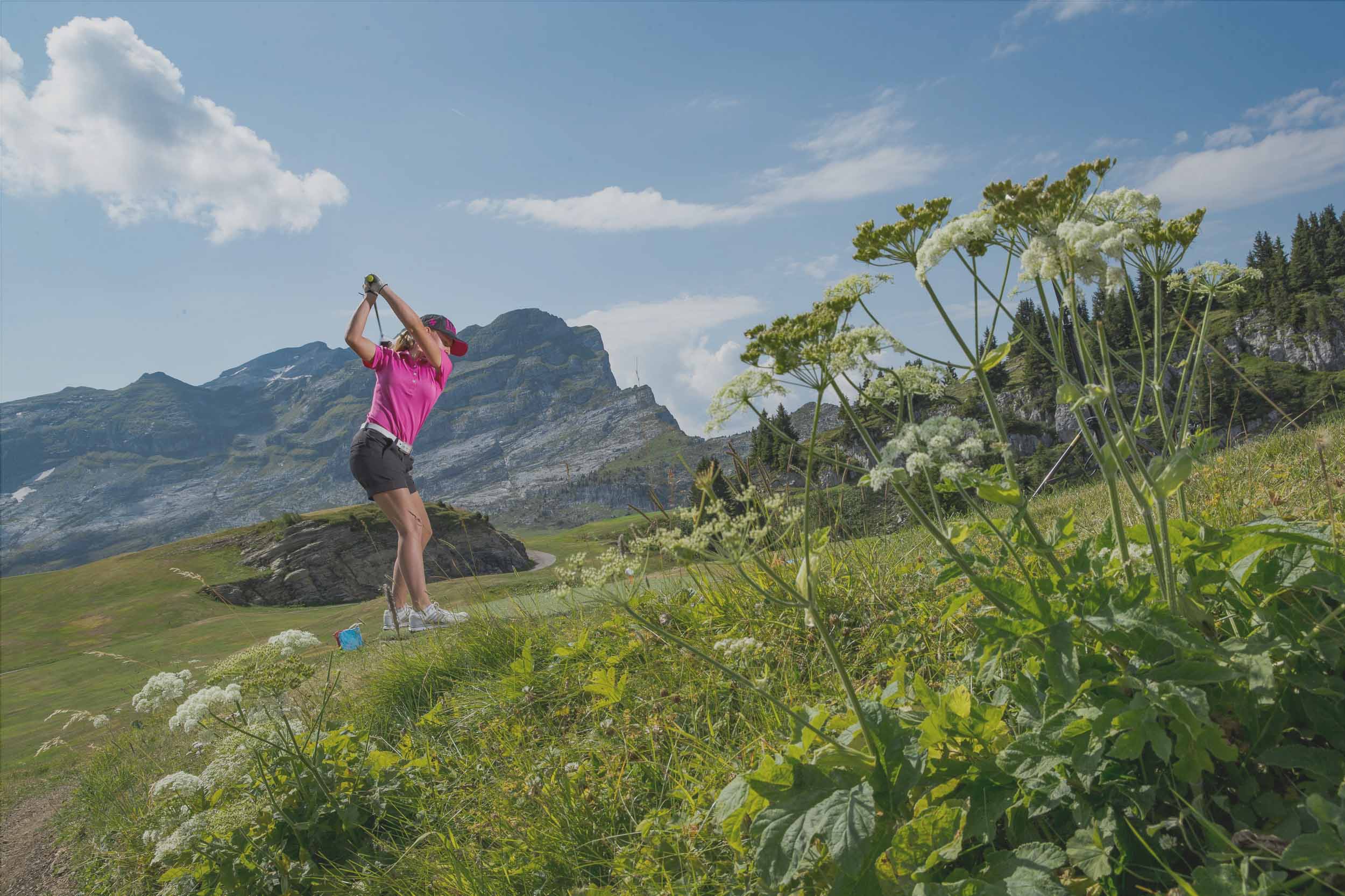 Een golfer in volle swing op een berggolfbaan, bij Golf de Flaine-Les Carroz, met de bergen van Aup de Véran op de achtergrond.