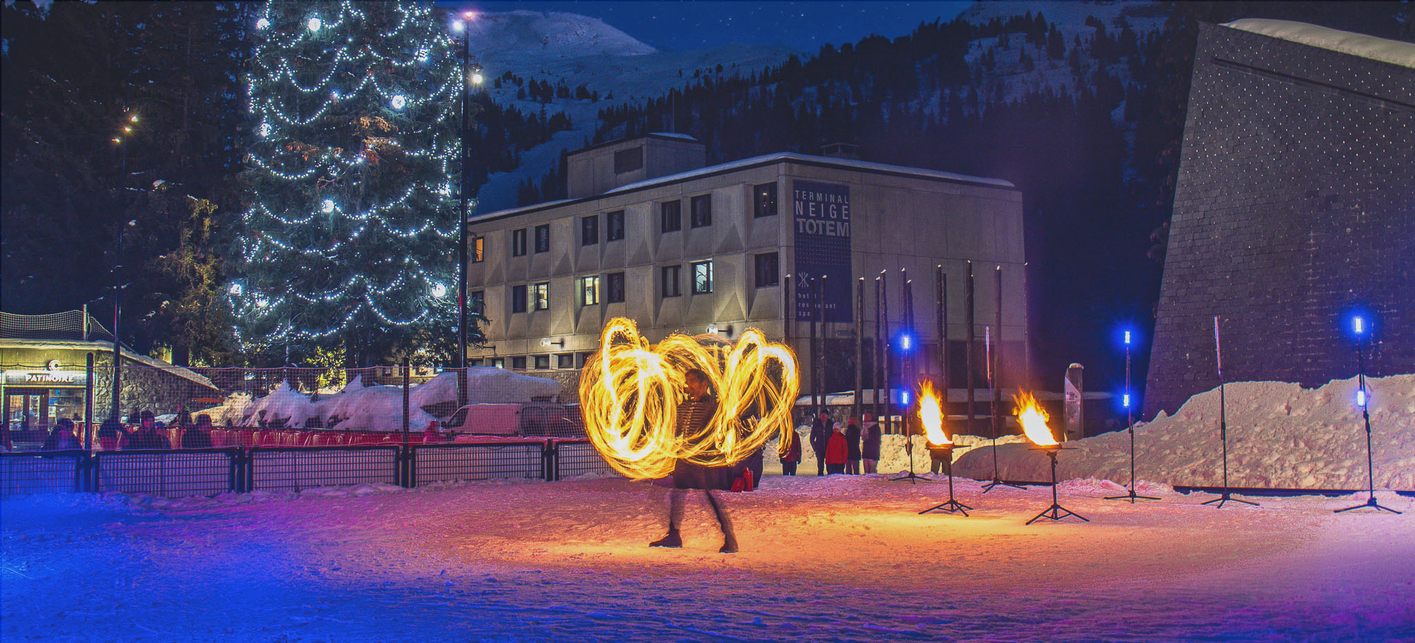 Foto van een nachtelijke vuurshow in Flaine, met vuurjongleurs en gekleurde lichten die het Forum verlichten onder een sterrenhemel.