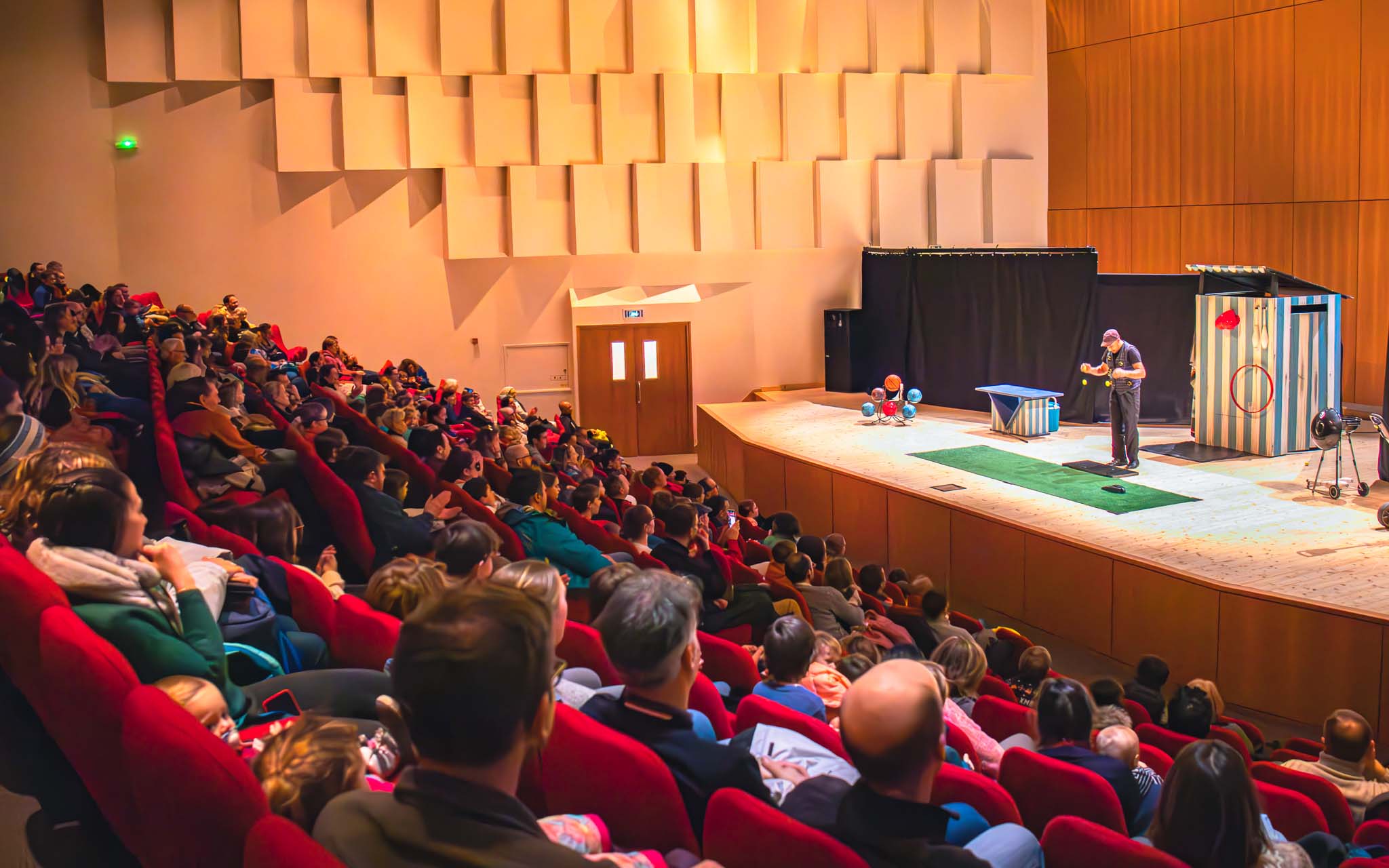 Binnenzicht van het Sylvie et Éric Boissonnas auditorium in Flaine, met een volle zaal en het podium bezet door een theatervoorstelling.