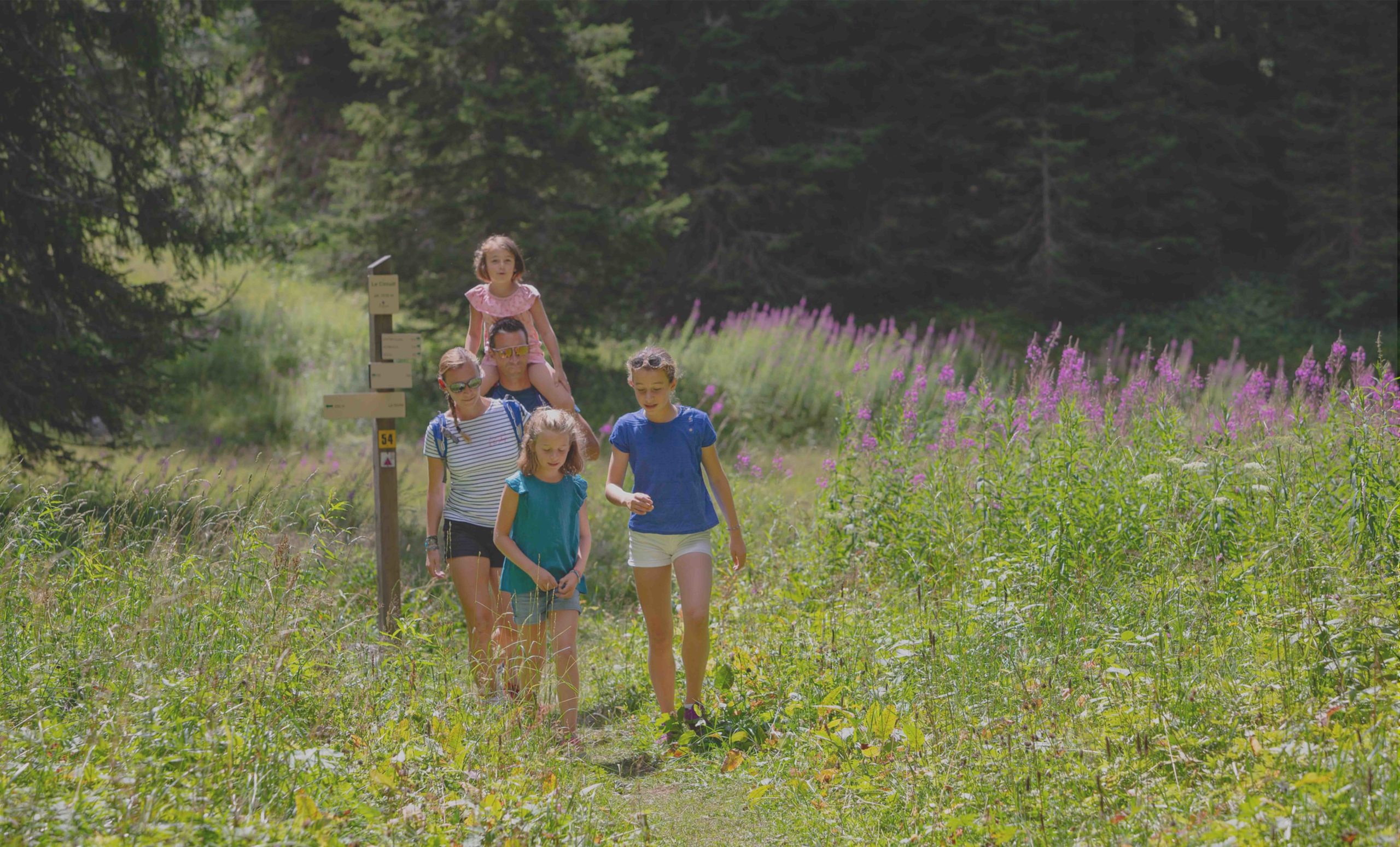 Une famille en randonnée sur un sentier fleuri à Flaine, entourée de nature et de forêts alpines.