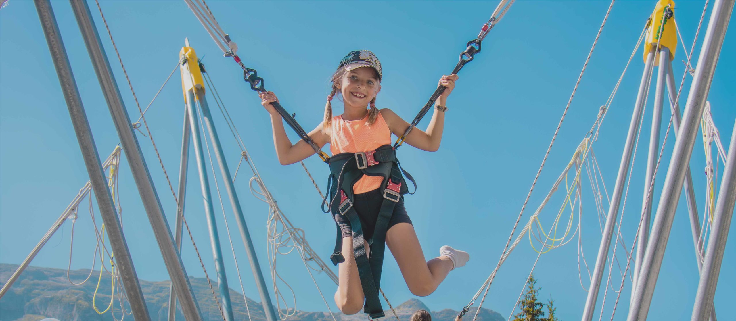 Een jong meisje doet een elasto bungeejump in het skioord Flaine, met de berg Aup de Véran op de achtergrond onder een blauwe hemel, dankzij de Flaine Zomerpas.