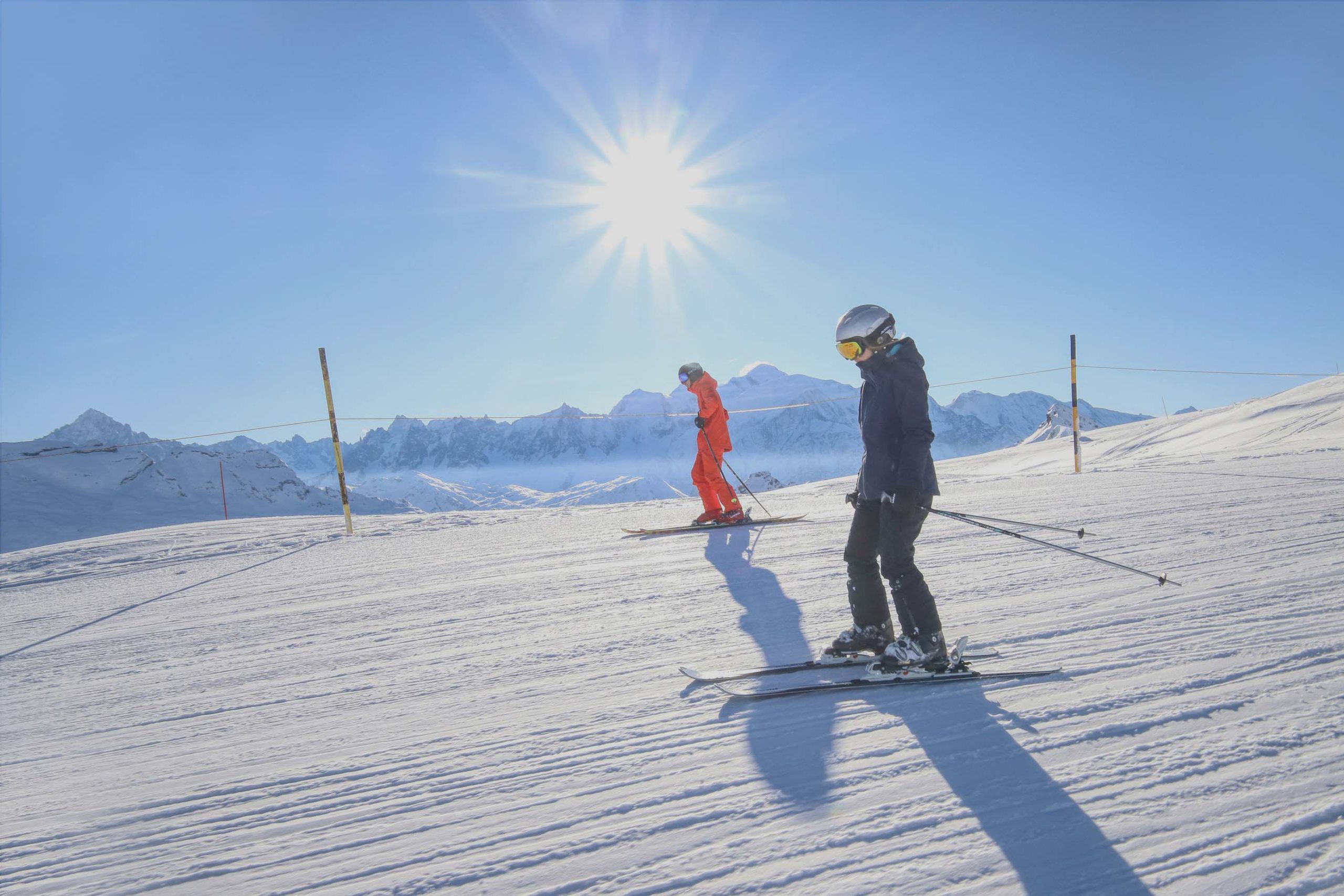 Deux skieurs au sommet des Grandes Platières à Flaine, en Haute-Savoie, avec le Mont Blanc en arrière-plan et un ciel bleu ensoleillé.