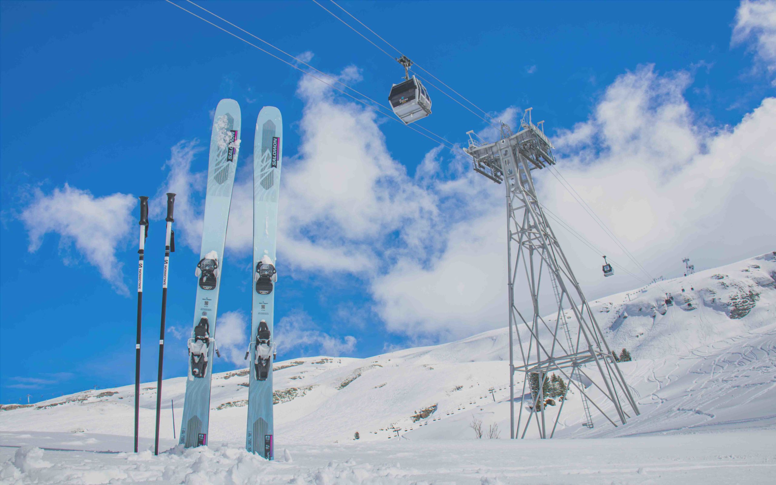 A pair of skis and ski poles stuck in the snow with the Grandes Platières cable car in Flaine passing over them.