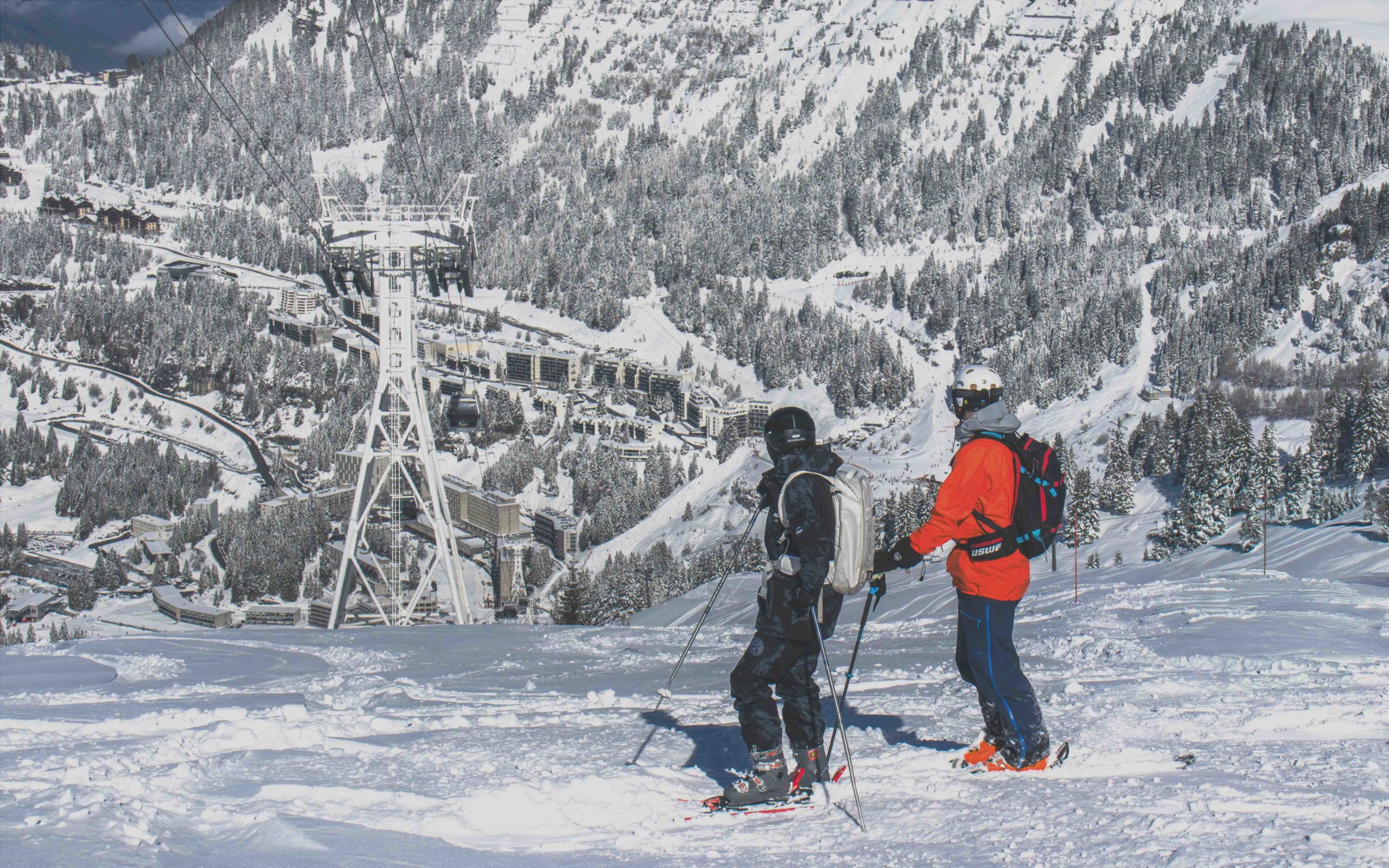 Two skiers in front of Flaine resort, with snow-covered buildings in the background.