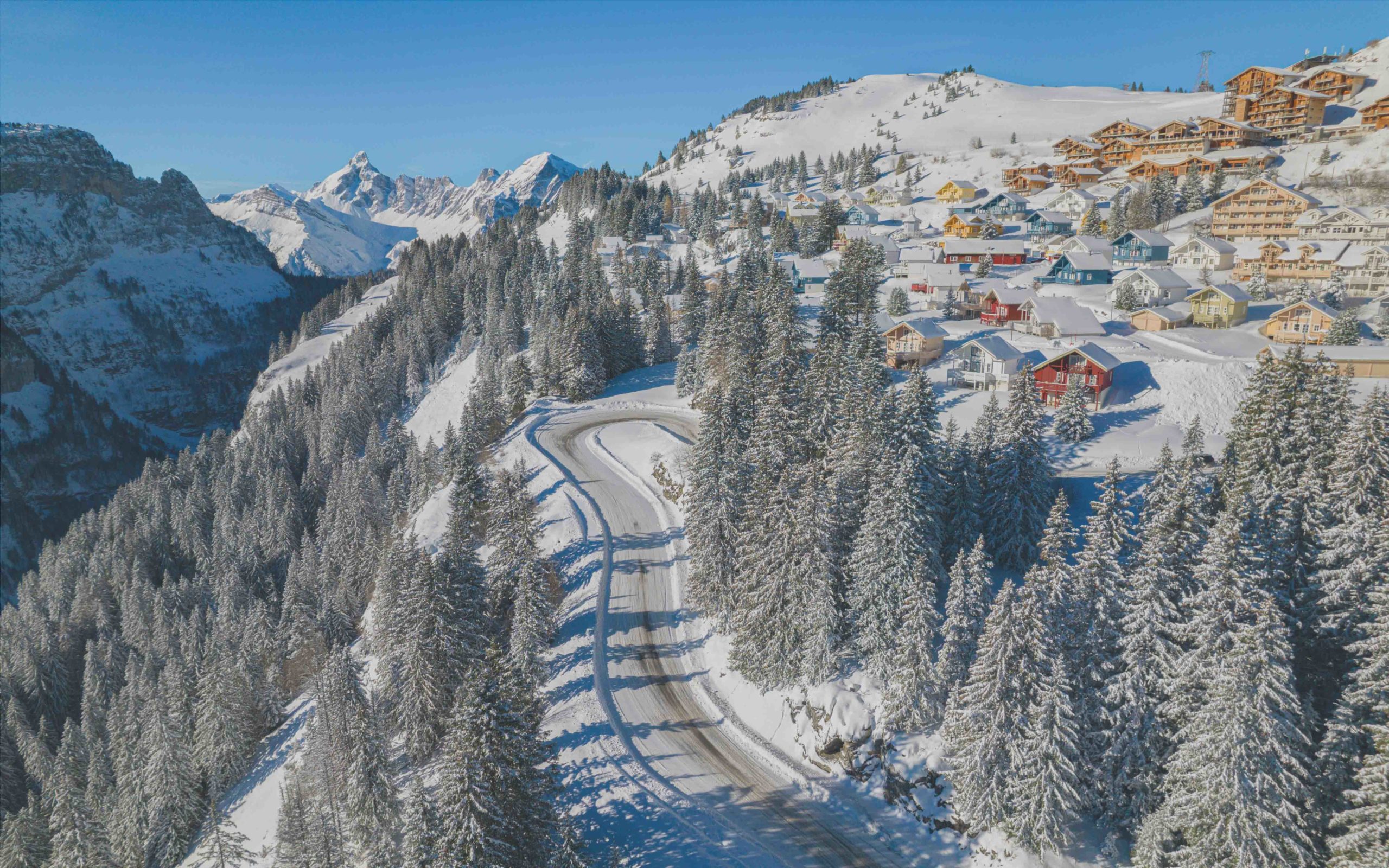 Route enneigée avec vue aérienne sur le Hameau de Flaine et la campagne environnante.