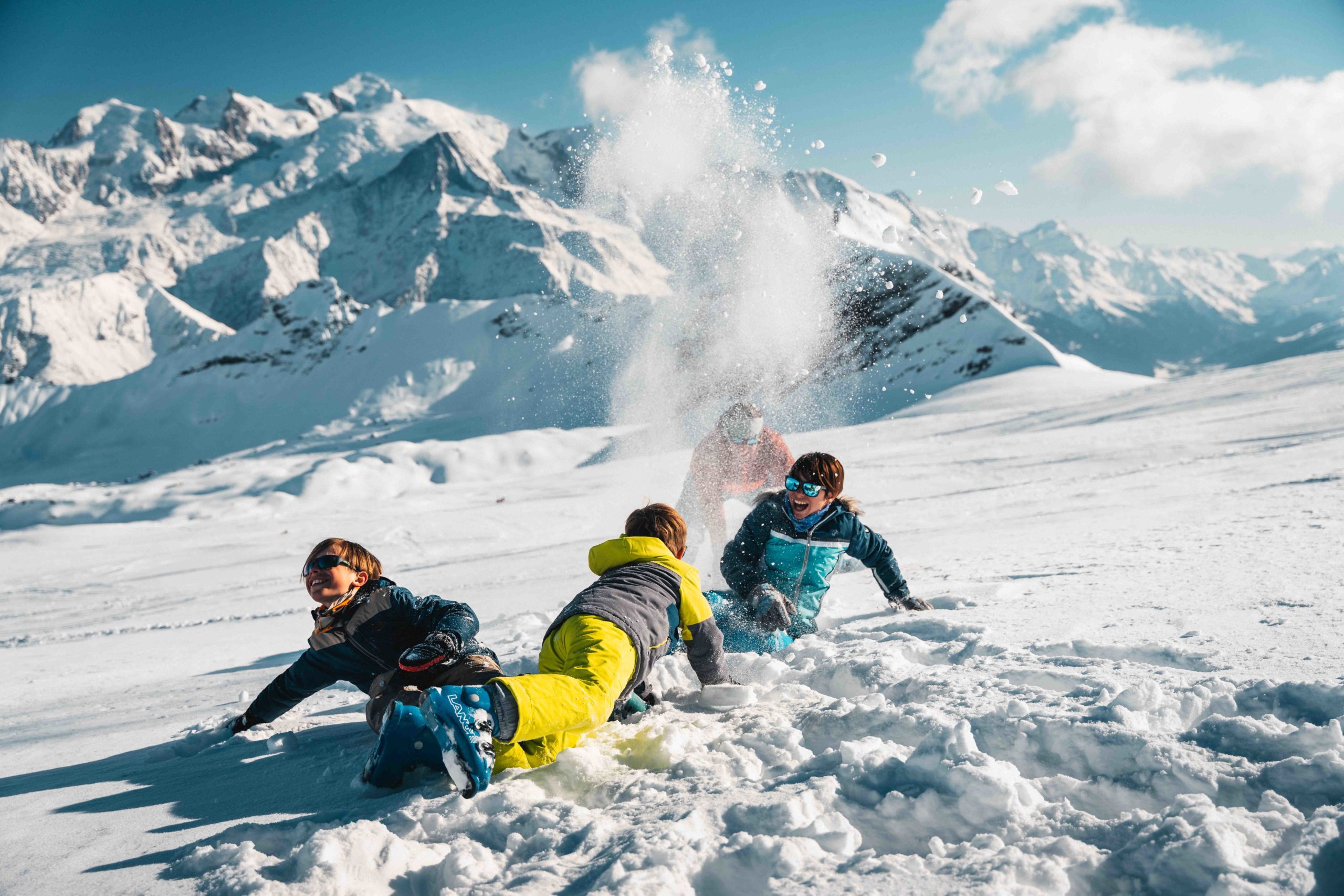 Flaine- Children in ski outfits laugh and play in the snow, with the snow-covered Mont Blanc in the background.