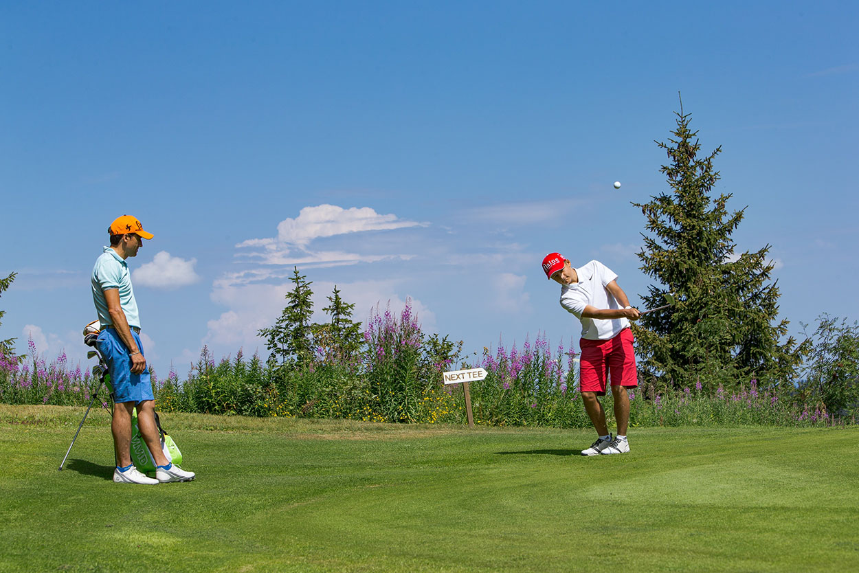 Deux golfeurs en action sur le green du parcours 18 trous du Golf de Flaine-Les Carroz, profitant d'une journée ensoleillée avec un ciel bleu dégagé.