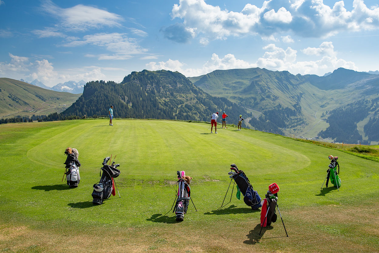 Golfers in action on the 18-hole course at Golf de Flaine-Les Carroz, under a blue sky, with a panoramic view of the Vallon de Flaine, the crests, Grand Vans and Tête Pelouse.