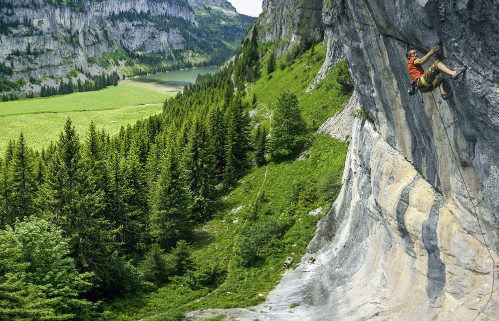 Un grimpeur escalade la dalle de l'Oiseau Rare à Flaine, avec en arrière-plan le lac de Flaine et un paysage alpin magnifique.