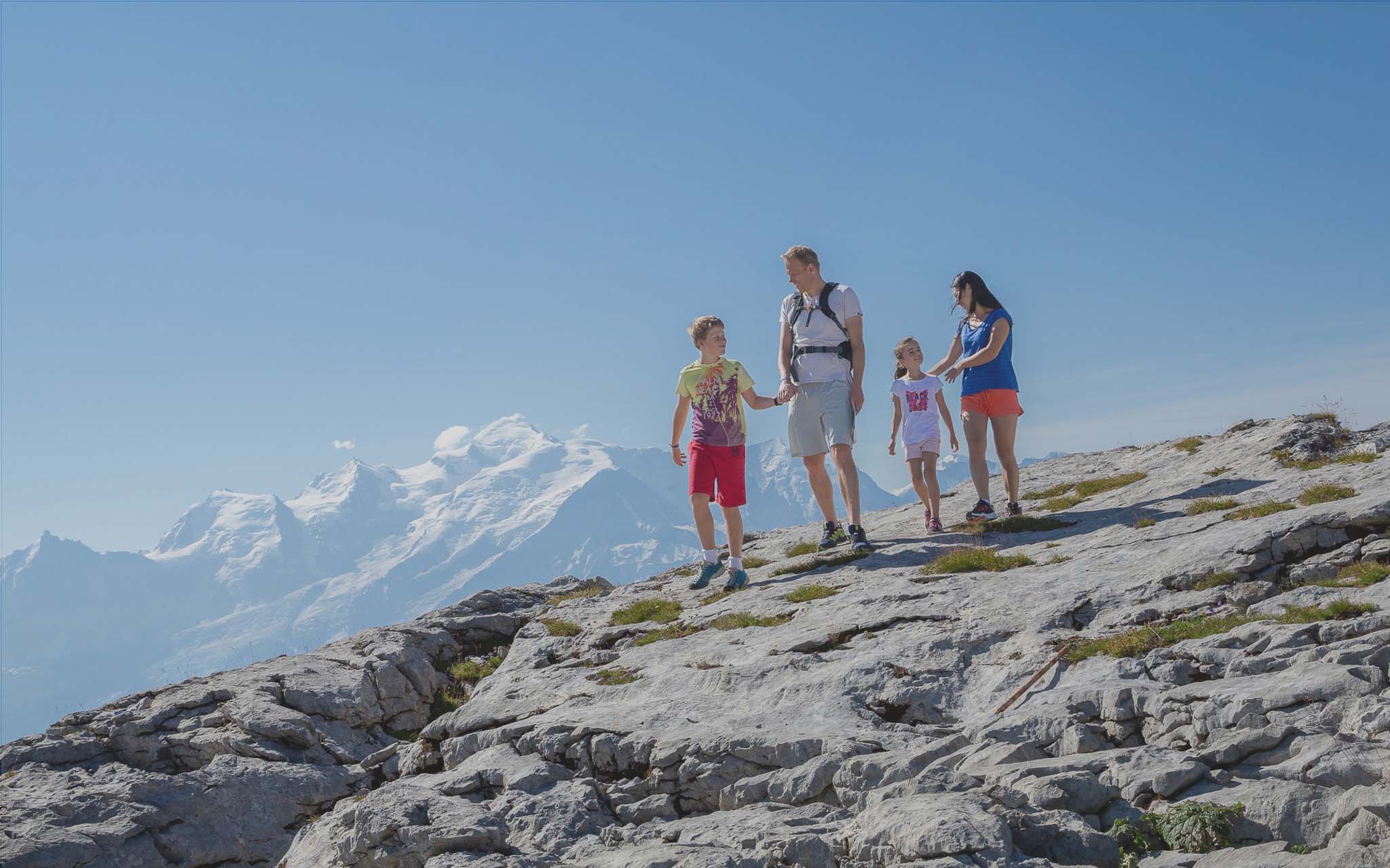 Wandelen met het gezin op de Désert de Platé in Flaine, met de besneeuwde toppen van de Mont Blanc aan de horizon onder een stralend blauwe hemel.