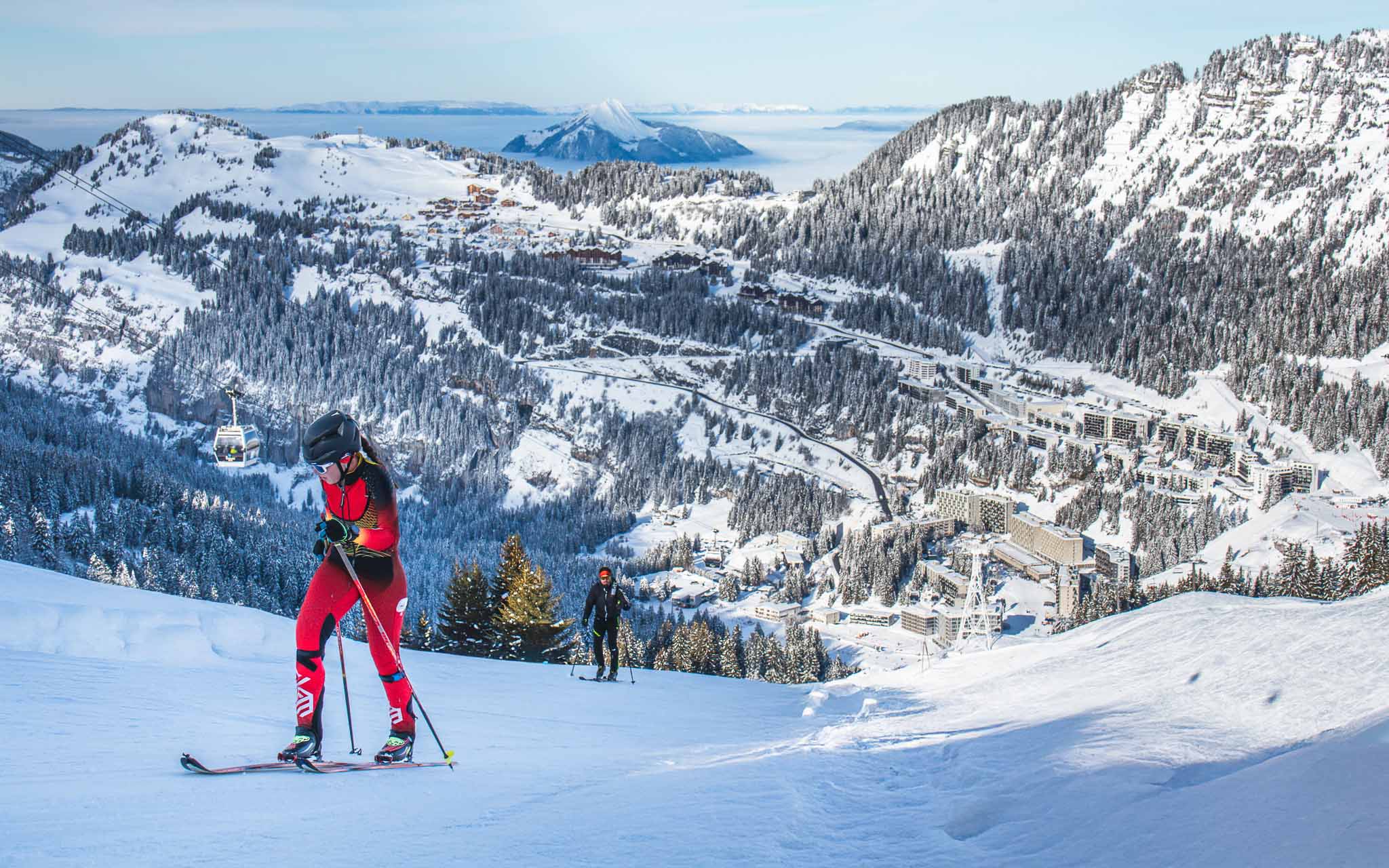 Skitoerers beklimmen een besneeuwde route, met het Flaine skigebied eronder zichtbaar.