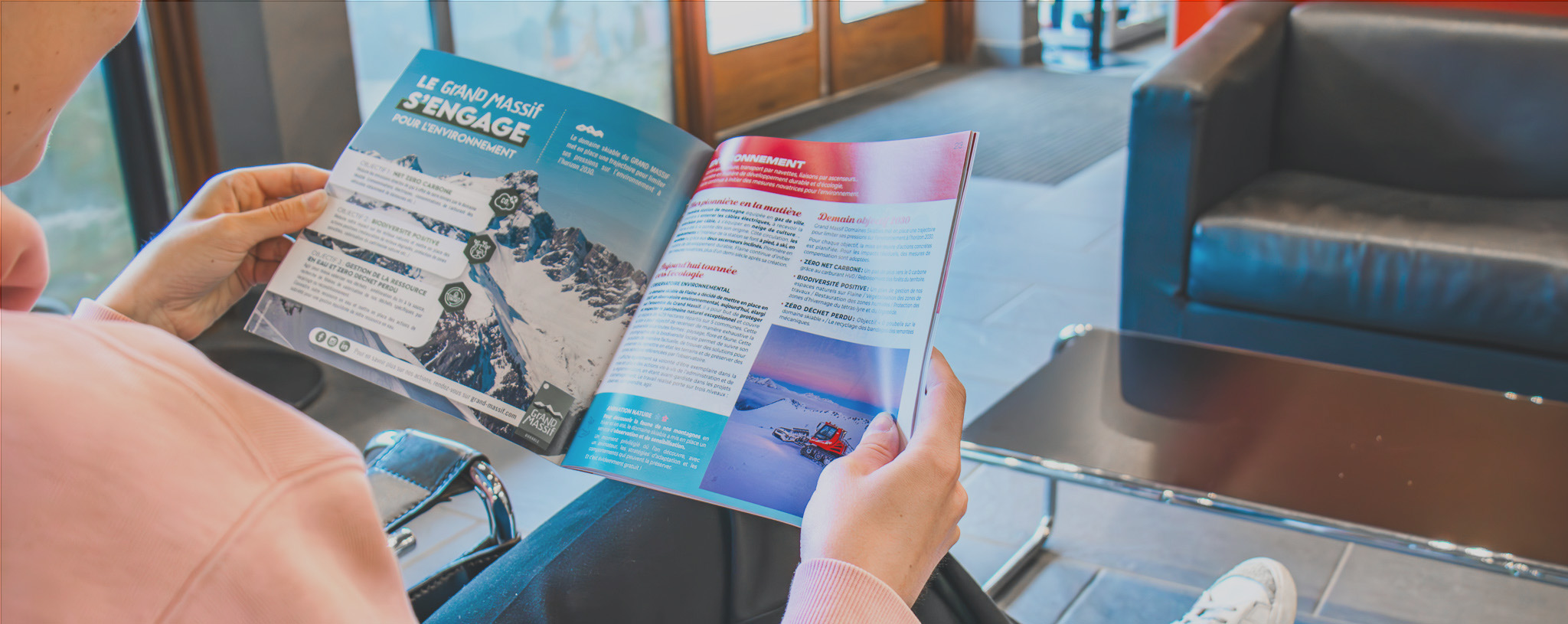 Personne assise dans un espace d'accueil, lisant une brochure d'information sur la station de Flaine, avec des détails sur les activités et les engagements de la station.