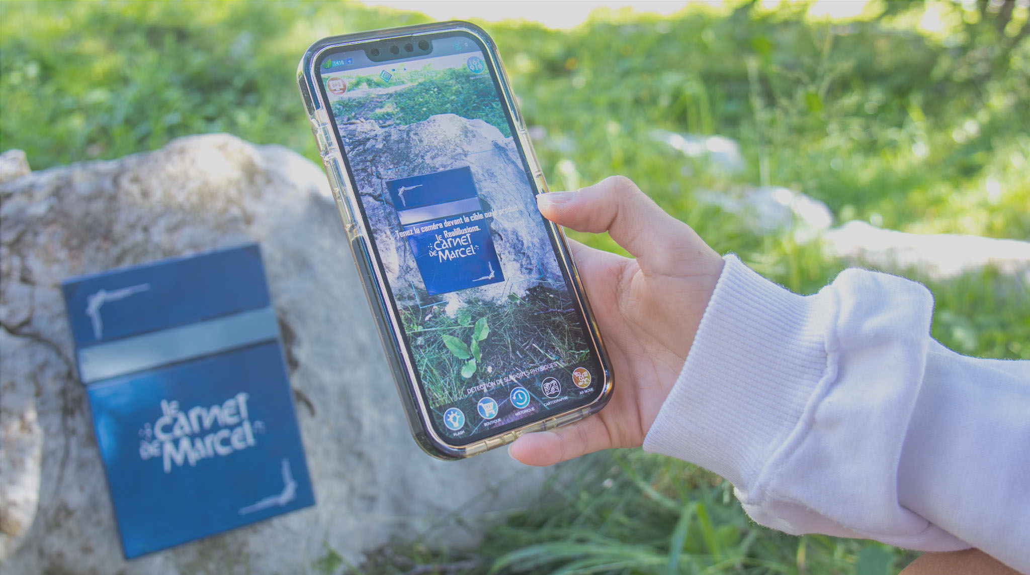 A child holds a smartphone in front of a sign on the ‘Le Carnet de Marcel’ theme trail in Flaine, combining nature and technology to discover the local heritage.