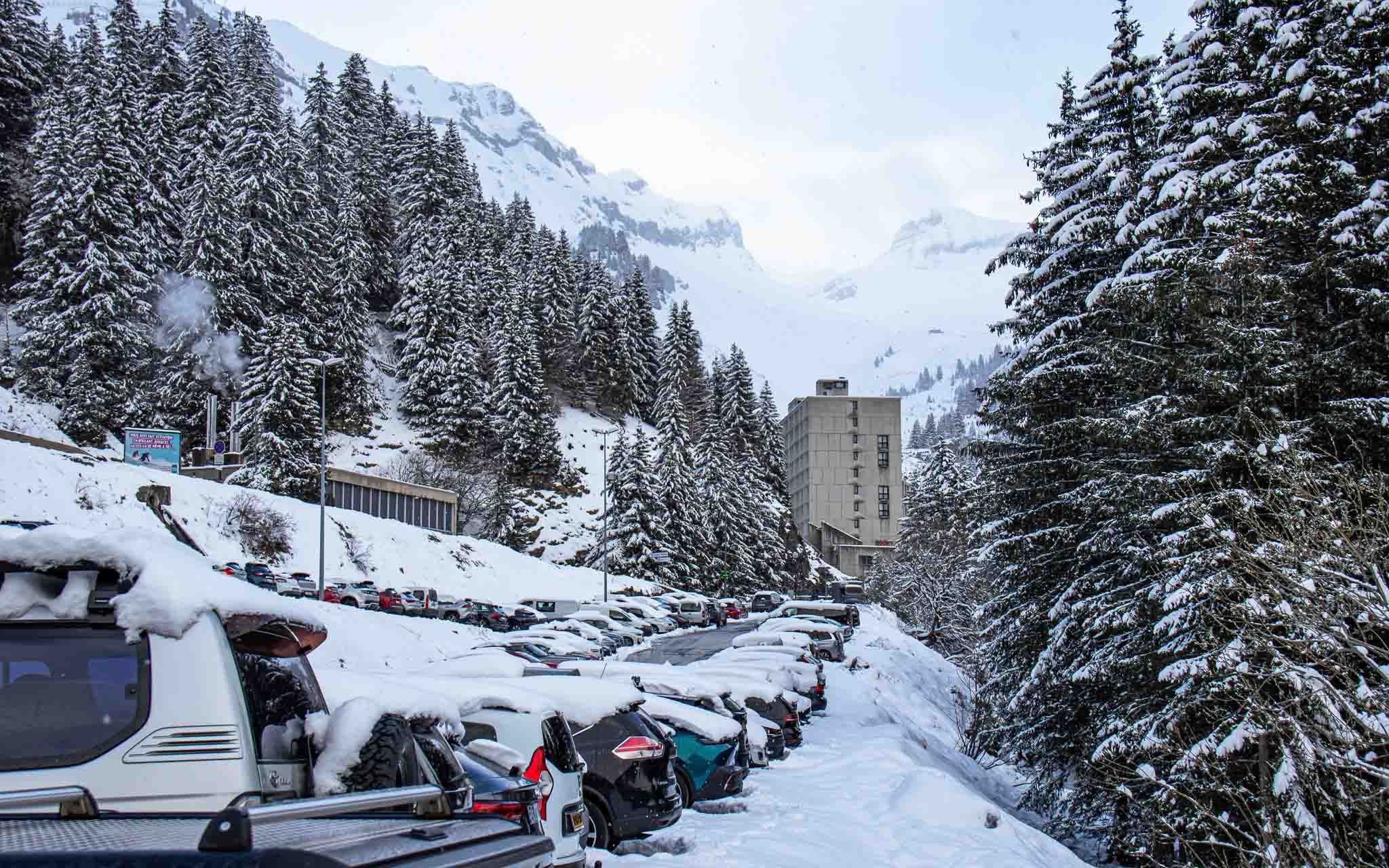 Besneeuwde parkeerplaats P2 voor de ingang van Flaine Forum, het skigebied van Flaine in de Haute-Savoie, omringd door dennenbomen en bergen.