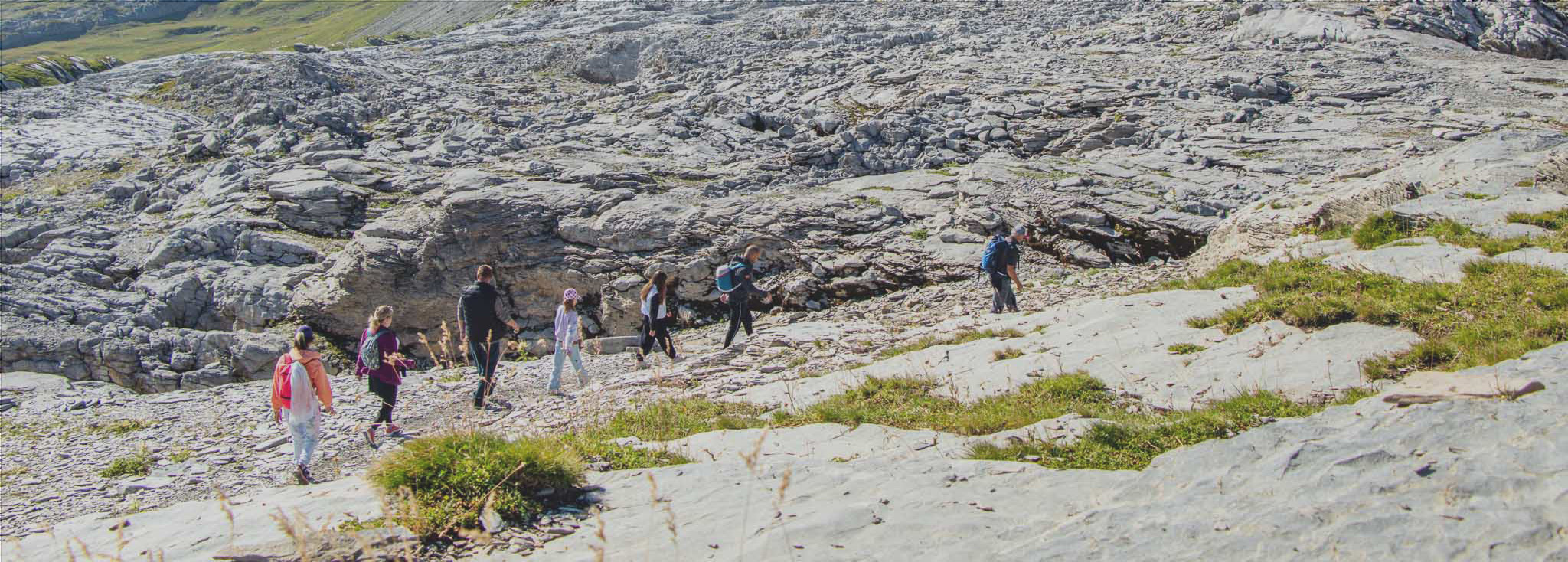 Un groupe de randonneurs accompagné d'un guide marche sur le Désert de Platé à Flaine, un paysage montagneux rocheux unique.